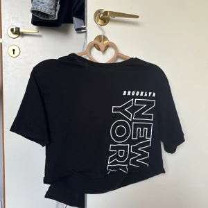 Svart croppad t-shirt med tryck från H&M - Svart croppad t-shirt från H&M med stort vitt tryck på framsidan där det står 'Brooklyn New York'. T-shirten storlek 146-152 10-12 