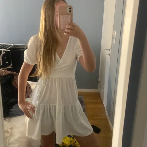 Vit omlottklänning  - Superfin vit kortklänning från Gina Tricot med omlottmodell och puffärmar. Klänningen har knyt i midjan och volang nertill, perfekt för sommarens alla tillfällen. Lätt och luftig i materialet.