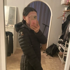 Svart lång dunjacka från Parajumpers - Säljer en svart lång dunjacka från Parajumpers i storlek XS. Jackan har huva, dragkedja framtill och ett broderat märke på ärmen. Lättviktig och figurnära modell som passar perfekt till kyliga dagar.