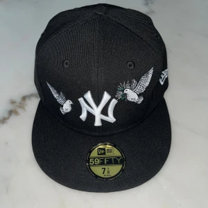 New Era Keps Svart - Det här är en svart New Era-keps med unik design: små fåglar pryder kepsen och ger den ett stilrent men ändå lekfullt uttryck. Kepsen är i storlek 56, men den passar även ett huvudomfång på cirka 57 cm tack vare en något flexibel passform. Perfekt för dig som gillar detaljer och vill sticka ut med en subtil men iögonfallande accessoar. Beställd direkt från USA.