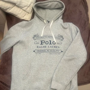 Grå hoodie från Polo Ralph Lauren - Snygg grå hoodie från Polo Ralph Lauren med tryck i mörkblått framtill. Tröjan har huva med vita snören och en stor magficka. Perfekt för en avslappnad och sportig stil. Pris kan diskuteras vid snabb affär!