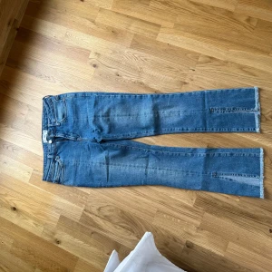 Blå jeansbyxor från Mango - Säljer ett par klassiska blå jeans från Mango med raka ben och råa kanter nertill. Byxorna har fem fickor, dragkedja och knapp framtill. Perfekta för en avslappnad stil.