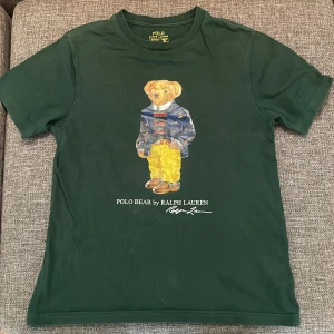 Ralph Laurent t-shirt - Mörkgrön t-shirt från Ralph Lauren med klassiskt Polo Bear-motiv på bröstet. T-shirten har rund halsringning och korta ärmar. Perfekt för dig som gillar stilrena plagg med en lekfull touch.