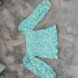 Blommig blus med smock från FB Sister - Säljer en söt blommig blus från FB Sister i storlek XS. Blusen har smockad kropp, långa puffärmar med resår och ett blått, grönt och vitt blommönster. Perfekt för vår och sommar!🌼🌸🌻🩷