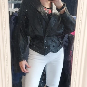 Vintage oversized skinnjacka med nitar - Cool svart skinnjacka med breda slag, markerad midja och dekorativa nitar och stjärnor på axlar och ärmar. Jackan har stora knappar framtill och en oversized passform som ger en edgy look.