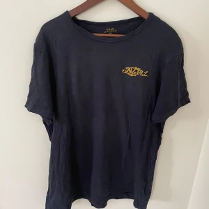 Svart t-shirt från Polo Ralph Lauren - Säljer en svart t-shirt från Polo Ralph Lauren med gul broderad logga på bröstet. Klassisk rund halsringning och korta ärmar. Perfekt för en stilren och enkel look.