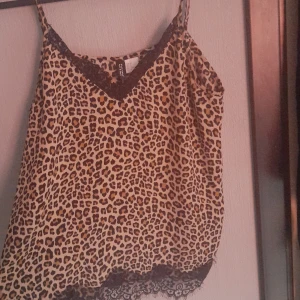 Leopardmönstrad linnetopp med spets från H&M Divided - Säljer en leopardmönstrad linnetopp från H&M Divided i storlek L. Toppen har tunna axelband, svarta spetsdetaljer vid halsringning och nederkant samt en v-ringad form. Perfekt för att addera lite edge till din outfit eller att använda att sova i! 
