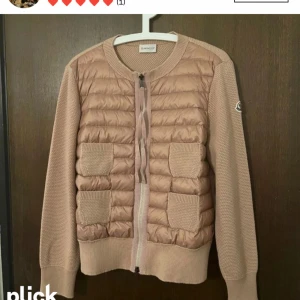 Beige cardigan jacka från Moncler - Snygg beige cardigan jacka från Moncler med quiltad framsida och stickade ärmar. Jackan har dragkedja framtill, två fickor med ribbade detaljer och Moncler-logga på ärmen. Perfekt för lager-på-lager under höst och vår.