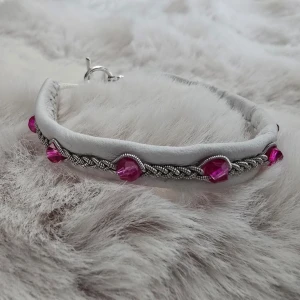 Vitt armband med rosa pärlor och tenntråd - Unikt armband i vitt skinn med flätad tenntråd och rosa pärlor. Stängs med ett snyggt silverfärgat T-lås. Perfekt accessoar för att ge din outfit en färgklick. Handledsmått 15,5-17cm 