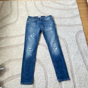Blå jeans från Jack & Jones - Säljer ett par klassiska blå jeans från Jack & Jones i storlek 34. Jeansen har slitna detaljer och hål på benen för en trendig look. De har normal passform och raka ben. Perfekta för dig som gillar en avslappnad stil. Kom privat för flera bilder