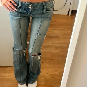 Lågmidjade bootcut jeans med slitningar - Snygga blå jeans med låg midja och bootcut passform. Jeansen har slitna detaljer vid knäna och längs benen för en trendig look. Klassisk femficksmodell med knapp- och dragkedjestängning framtill. Klicka gärna på köp nu💋