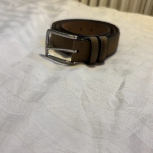 Brunt bälte från Dan John med silverfärgat spänne - Snyggt brunt bälte från Dan John med klassiskt silverfärgat spänne. Bältet har stilrena sömmar och är gjort i skinn med en slät yta. Perfekt accessoar för att lyfta din outfit.