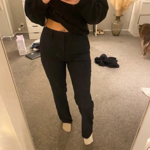 Svarta kostymbyxor med smala ränder från Madlady - Använd 1 gång, Snygga svarta kostymbyxor från Madlady med diskreta vita smala ränder. Byxorna är högmidjade och har en rak passform med hällor för bälte och klassisk dragkedja framtill. Perfekta för en stilren look.