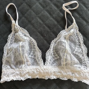Vit spets bralette från Gina Tricot - Säljer en superfin vit bralette från Gina Tricot i spets. Den har tunna axelband och vacker spetsdetalj över hela toppen. Perfekt för lager-på-lager eller som den är under en skjorta.