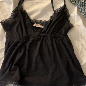 Svart spetslinne från Nelly - Säljer ett svart linne från Nelly med spetsdetaljer längs urringningen och axelband. Linnet har en v-ringad form och tunna axelband, perfekt för lager-på-lager eller som det är.