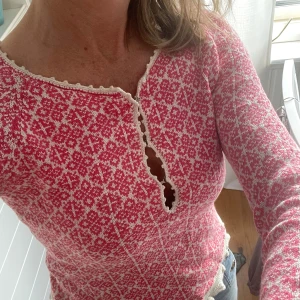 Rosa och vit stickad kofta från Odd Molly - Superfin rosa och vit stickad kofta från Odd Molly med dekorativt mönster, knytband i midjan och broderad logga på ryggen. Koftan har lång ärm, v-ringning med spetskant och knappar framtill.