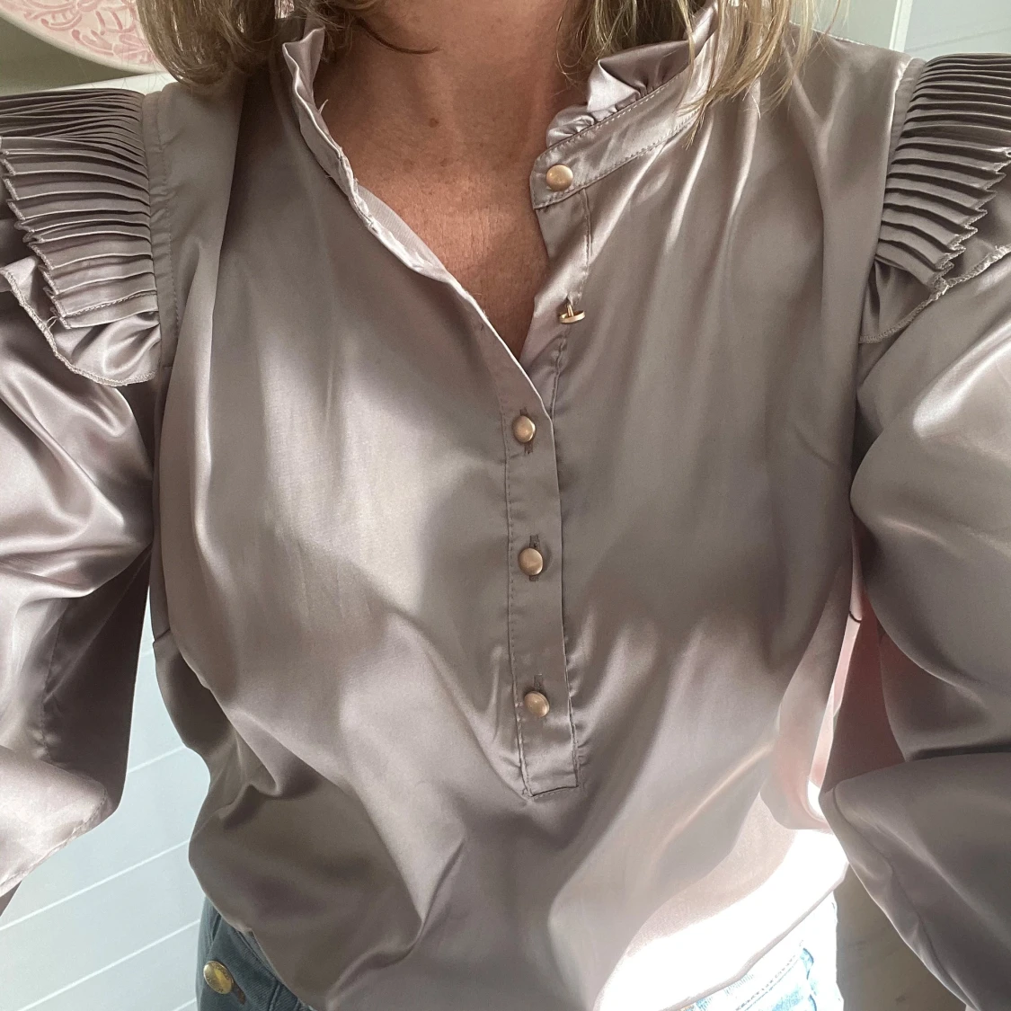 Beige blus med puffärmar och plisserade axlar, guldfärgade knappar och trekvartsärmar.