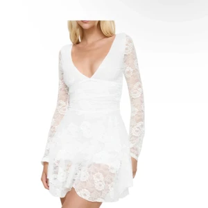 Vit spetsklänning med djup v-ringning - Superfin vit kortklänning i spets med långärmade ärmar och djup v-ringning. Klänningen har öppen rygg med knytband och volangig kjol. Perfekt för somriga tillfällen eller studentfirande. Lite liten i storleken så om du vanligtvis har storlek S är denna bra. 