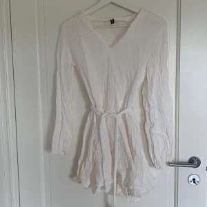 Vit klänning med knyte - Använd 1 gång, har en sminkfläck som inte syns när man har den invikt vid v-ringningen, har även gått upp lite längst nere i v-ringningen. Annars fint skick! 