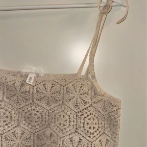 Beige virkad croppad linnetopp från H&M - Superfin beige croppad linnetopp från H&M med virkade detaljer och knytbara axelband. Perfekt till sommaren och ger en bohemisk känsla med sitt mönstrade virkade material.