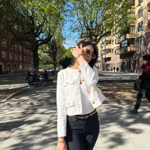 Vit kort kavajjacka med guldknappar - Säljer en snygg vit kavajjacka med guldknappar och fickdetaljer framtill. Jackan är croppad och har lång ärm, perfekt för att lyfta en outfit. Klassisk och stilren design som passar till mycket.