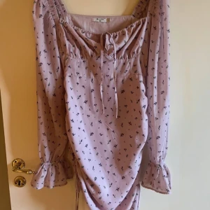 Ljuslila blommig klänning från NA-KD - Supersöt ljuslila klänning från NA-KD med små blommor, långa ärmar med volang vid ärmslut och knyt framtill. Perfekt nu till våren/sommaren💜🌸