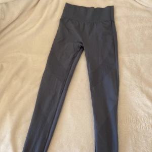 Blå träningstights från Lager 157 - Säljer ett par blå träningstights från Lager 157 med hög midja och ribbade detaljer. Tightsen är stretchiga och sitter tight, perfekta för gym eller yoga. Materialet är syntet och de har en sömlös design för extra komfort.