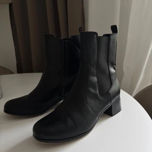 Svarta boots med klack - Säljer ett par svarta chelsea boots i skinnimitation med medelhög klack och rund tå. Skorna har resår på sidorna och dragkedja på insidan för enkel påtagning. Perfekta för en stilren look.                                         Använda en gång i ca 2h.