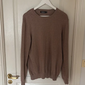 Brun bomullströja från Dressmann - Säljer en klassisk brun långärmad tröja från Dressmann i mjuk bomull. Enkel och stilren design med rund halsringning och ribbade muddar vid ärmslut och nederkant. Perfekt för lager-på-lager eller som den är.