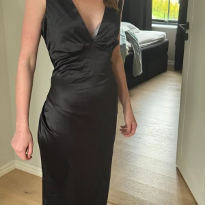 Svart långklänning med v-ringning - Säljer en elegant svart  långklänning. Klänningen har breda axelband och är tillverkad i ett glansigt material som ger en lyxig känsla. Perfekt för speciella tillfällen🤩🫶🏼