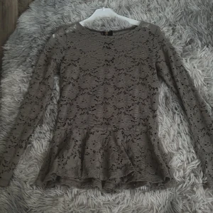 Beige spetsblus med volang - Säljer en beige långärmad blus i spets med volang nertill. Blusen har rund halsringning och dragkedja i ryggen. Perfekt för dig som gillar romantiska detaljer och en feminin stil. Finns ingen storleks lapp men den är i storlek S.
