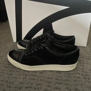 Svarta sneakers från Lanvin - Säljer ett par stilrena lanvin med glans i bra skick förutom de slitaget på bild 2. Har precis satt på helt nya snören och det medföljer box. Det är bara att skicka ett dm vid frågor eller funderingar.