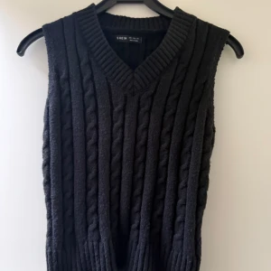 Svart stickad väst från SHEIN - Svart kabelstickad väst från SHEIN med v-ringning och bred ribbad kant vid hals och nederdel. Perfekt att styla över en skjorta eller t-shirt för en trendig lager-på-lager-look. Nästintill helt ny och har inga defekter osv.