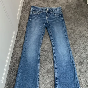 Blå bootcut jeans från Gina Tricot - Snygga blå jeans från Gina Tricot i storlek 152. Klassisk femficksmodell med bootcut-ben och normal passform. Jeansen har ljus tvätt och tydliga sömmar, perfekta för en avslappnad stil.