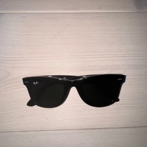 Svarta solbrillor från Ray-Ban - Klassiska svarta solglasögon från Ray-Ban med Wayfarer-form. Inte särskilt använda. Bågarna är tillverkade i blank svart plast och har mörka glas. Har ej kvar kvittot.