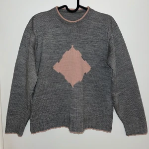 Grå stickad tröja - En 90s vintage grå stickad tröja med stor rosa diamantformad detalj. Tröjan har långa ärmar och rosa kanter vid hals, ärmslut och nederkant. Passar även storleken 38 men kan bli lite för kort vid armlängderna. Slitstarkt material! 🌷