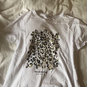 Vit t-shirt med leopardmönster från Monki - Vit t-shirt från Zara med tryck i leopardmönster i svart och gult på framsidan. Rund halsringning och korta ärmar. Texten 'New Print N°26' under trycket.