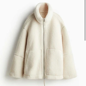 Vit teddyjacka med dragkedja - Säljer en vit teddyjacka med dragkedja framtill och stora fickor. Jackan har hög krage och är långärmad, perfekt för kyliga dagar. Supermjuk och trendig