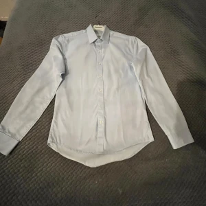 Ljusblå skjorta från Selected Homme - Säljer en stilren ljusblå skjorta från Selected Homme. Skjortan har en slim fit passform och är lätt att stryka. Perfekt för en snygg och enkel look. Den har långa ärmar och knappar framtill.