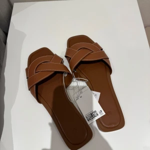 Bruna sandaler HM - Säljer ett par bruna sandaler från H&M med breda, flätade remmar och kontrastsömmar. Skorna har platt sula och öppen tå, perfekta för varma dagar. Enkla att ta på och av tack vare slip-in-modellen. Storlek 40 och helt nya! 🥰HELT SLUTSÅLDA