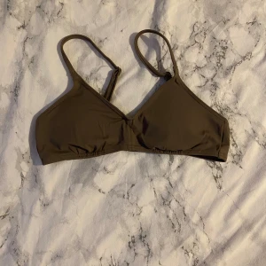 Brun bikiniöverdel med justerbara axelband - Säljer en stilren brun bikiniöverdel med smala, justerbara axelband och enkel knäppning bak. Modellen har en klassisk trekantsform med en tunn vaddering och är perfekt för strand eller pool.