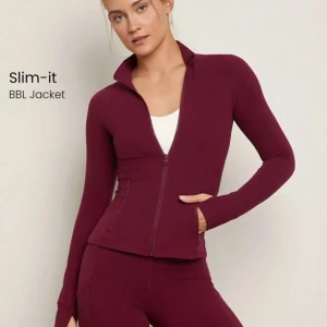 Vinröd träningsjacka med dragkedja - Slimmad vinröd träningsjacka med dragkedja framtill och hög krage. Jackan har långa ärmar och sitter tight mot kroppen. Perfekt för träning eller en sportig look.