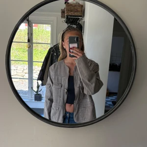 Grå utilityjacka med fickor - Säljer en grå utilityjacka med flera stora fickor framtill och på ärmarna. Jackan har dragkedja och knappdetalj vid halsen. Rak passform och tillverkad i ett kraftigare bomullstyg. Perfekt för en avslappnad och cool stil.