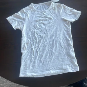 Vit basic t-shirt - En klassisk vit t-shirt med rund hals och korta ärmar. Perfekt att matcha med jeans eller shorts för en enkel och clean look. T-shirten är i ett mjukt material och har en normal passform.