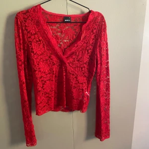 Röd spetsblus från Gina Tricot - Säljer en röd långärmad blus från Gina Tricot i genombruten spets med blommigt mönster. Toppen har v-ringning och är figurnära med transparent känsla. Perfekt för dig som vill sticka ut med en färgstark och feminin look.