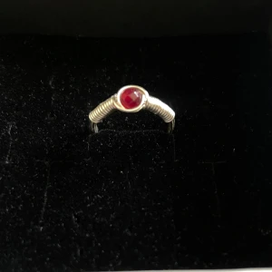 Silvrig ring med röd sten - Unik silvrig ring med en rund, röd sten i mitten. Ringen är handgjord av mig, i storlek S (16 mm i diameter) 