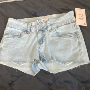 Ljusblå jeansshorts från Nelly - Snygga ljusblå jeansshorts från Nelly med rå kant och dubbla knappar framtill. Shortsen har klassiska fickor och coola rosa broderade detaljer på bakfickorna. Perfekt för sommarens alla äventyr, med en loose fit och fräscha vibbar. Aldrig andvända som du ser på prislappen. Köpta för 500 säljer för 400. Hör av dig vid eventuella frågor!