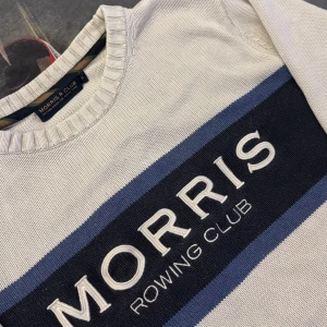 Stickad Morris Rowing Club tröja - Vit stickad tröja från Morris Rowing Club med blå och marinblå ränder över bröstet och broderad logga. Rund halsringning och ribbade muddar vid ärmslut och nederkant. Perfekt för en stilren look.