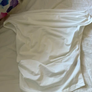 Två offshoulder korta klänningar - Säljer två stilrena offshoulder klänningar i kort modell, en i vit och en i ljusrosa. Båda är ärmlösa och har en enkel, tight passform med snygg drapering upptill. Perfekta för dig som gillar minimalistisk och trendig stil.