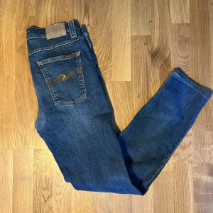 Nudie Jeans Lean Dean - Snygga blå jeans från Nudie Jeans, modell Lean Dean i färgen Bay Blue. Klassisk femficksdesign med gul söm på bakfickorna. Bra skick, det ända är att de blivit lagade i skrevet av Nudie själva. Inget man tänker på eller som påverkar funktionen.